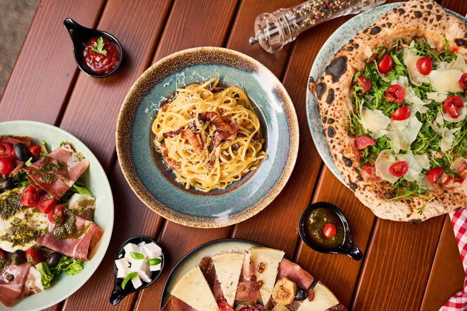 Pasta Carbonara, Pizza und Salate auf einem Holztisch